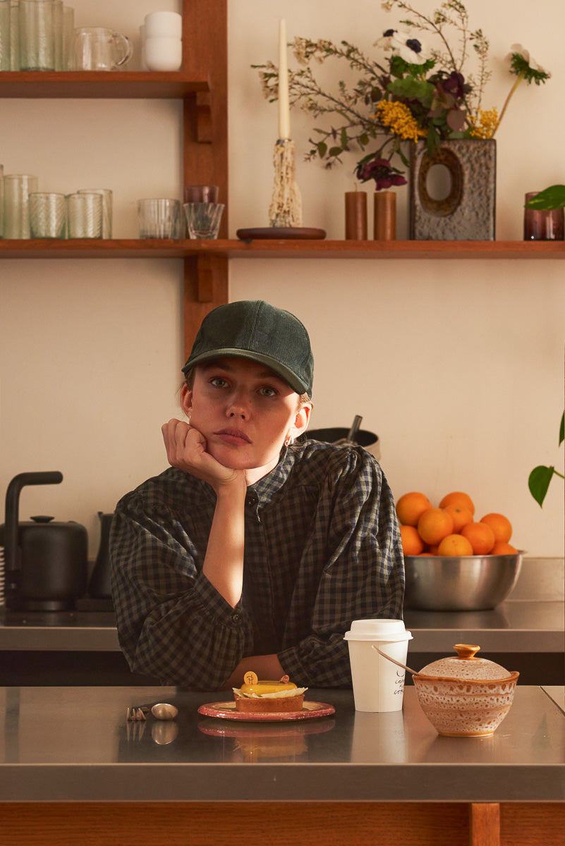 Portrait femme comptoir bar portant blouse vichy kaki Marlot Paris et casquette.