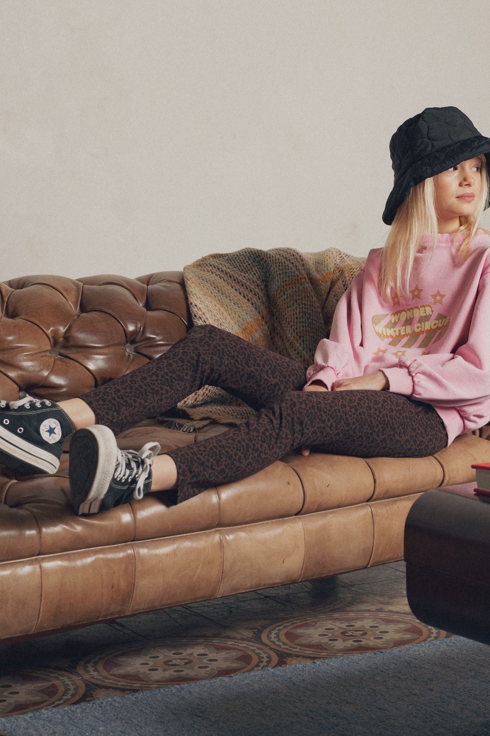 Fillette sur canapé cuir portant legging léopard brun et sweat rose Marlot Paris.