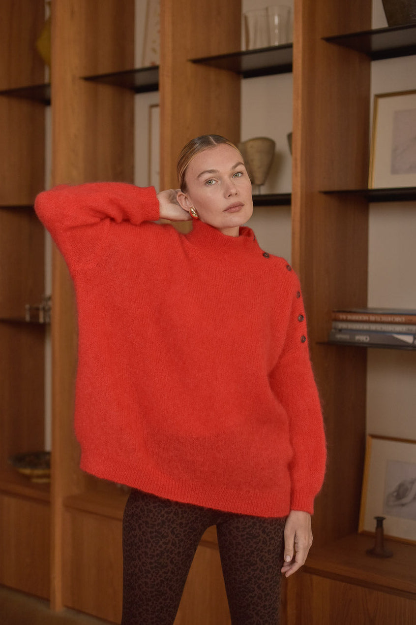 Portrait femme portant pull rouge mohair Marlot Paris devant bibliothèque.